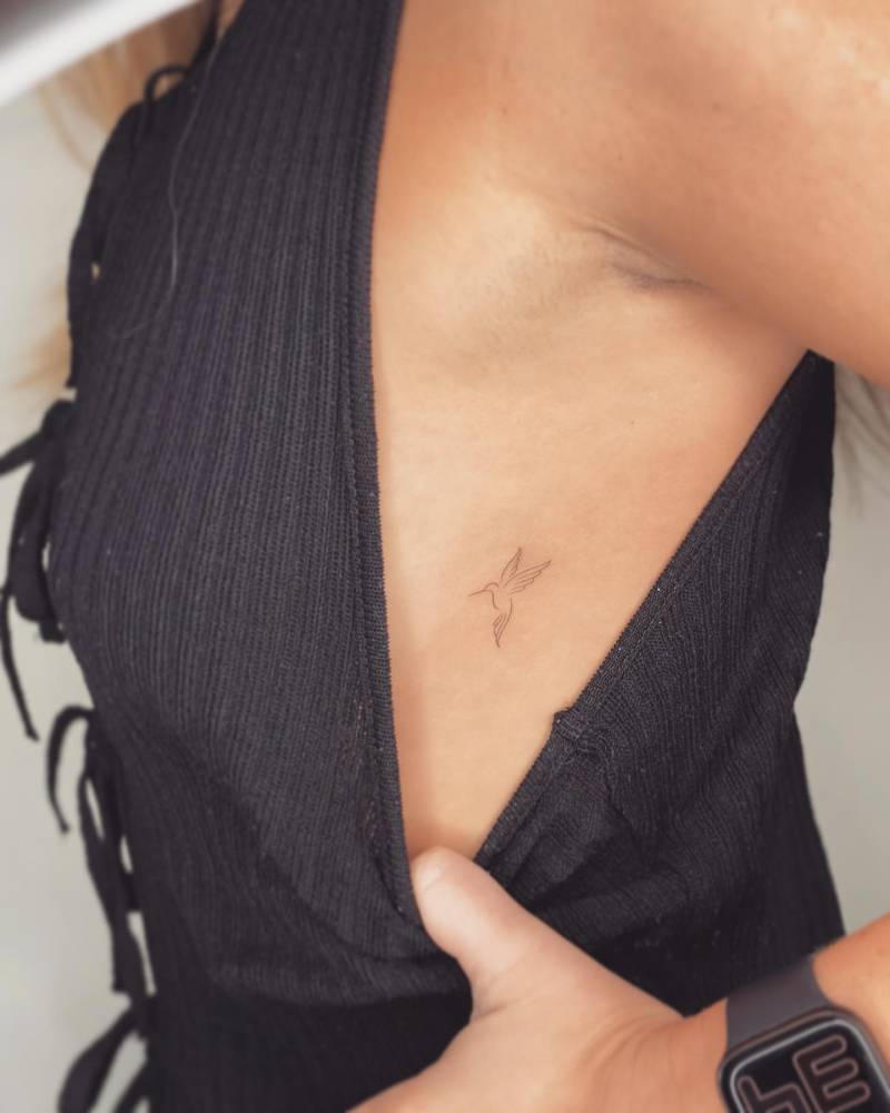 Fine line style hummingbird tattoo placed on the side boob.