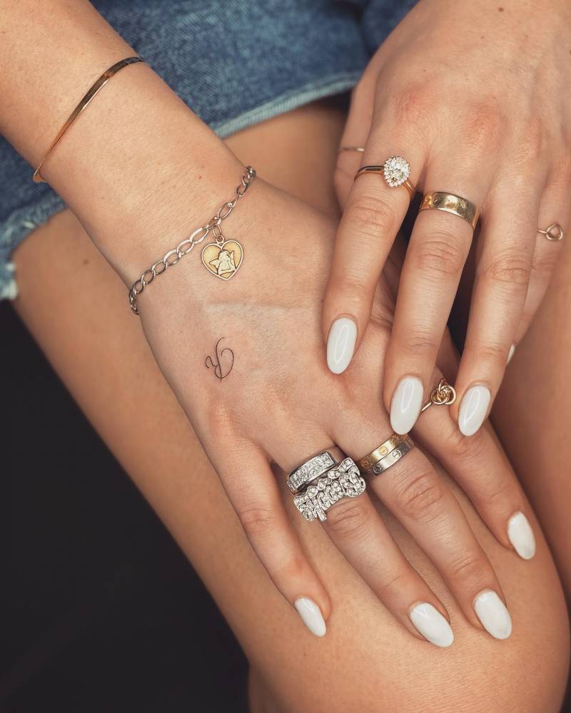 Tiny letter "R" tattoo located on the hand.