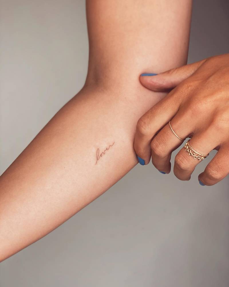 Tattoo of the word "lover" handwritten on the inner forearm.