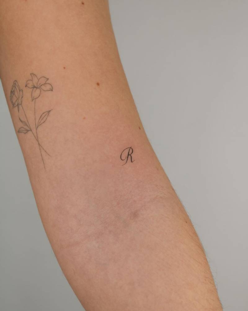 Tiny letter "R" tattoo located on the bicep.