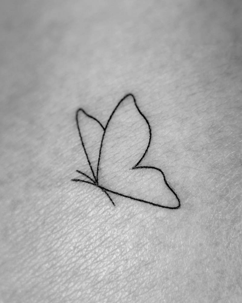 Minimalistic style butterfly tattoo located on the shoulder.