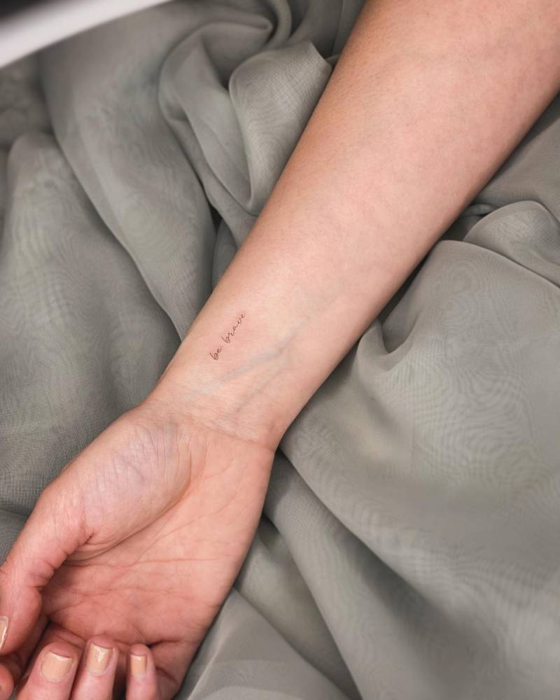 "Be brave" lettering tattoo handwritten on the wrist.
