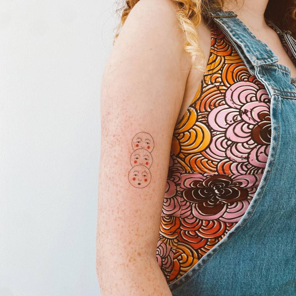 Hand poked moon faces tattooed on the upper arm.