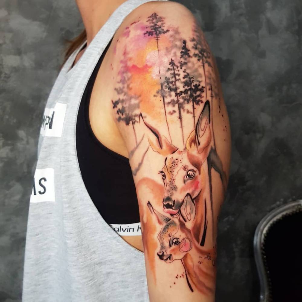 Watercolor deer tattoo locate don the upper arm.