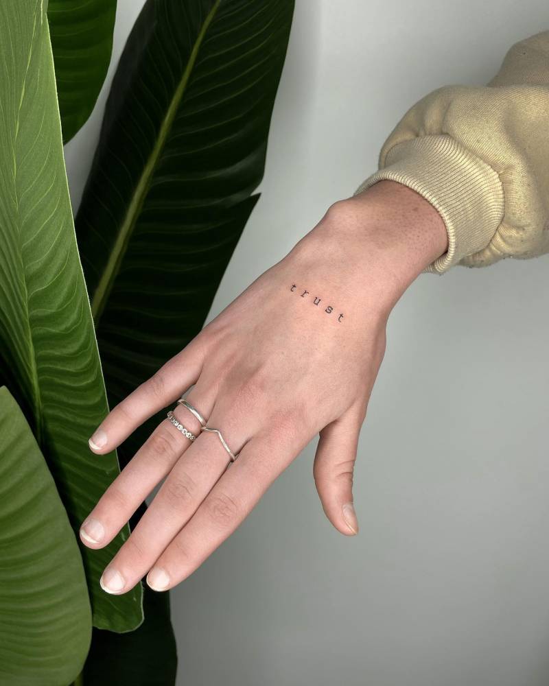 Tattoo of the word "trust" located on the hand.