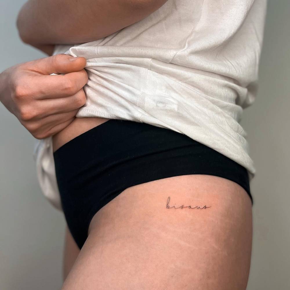 Tattoo of the word "bisous" handwritten on the hip.