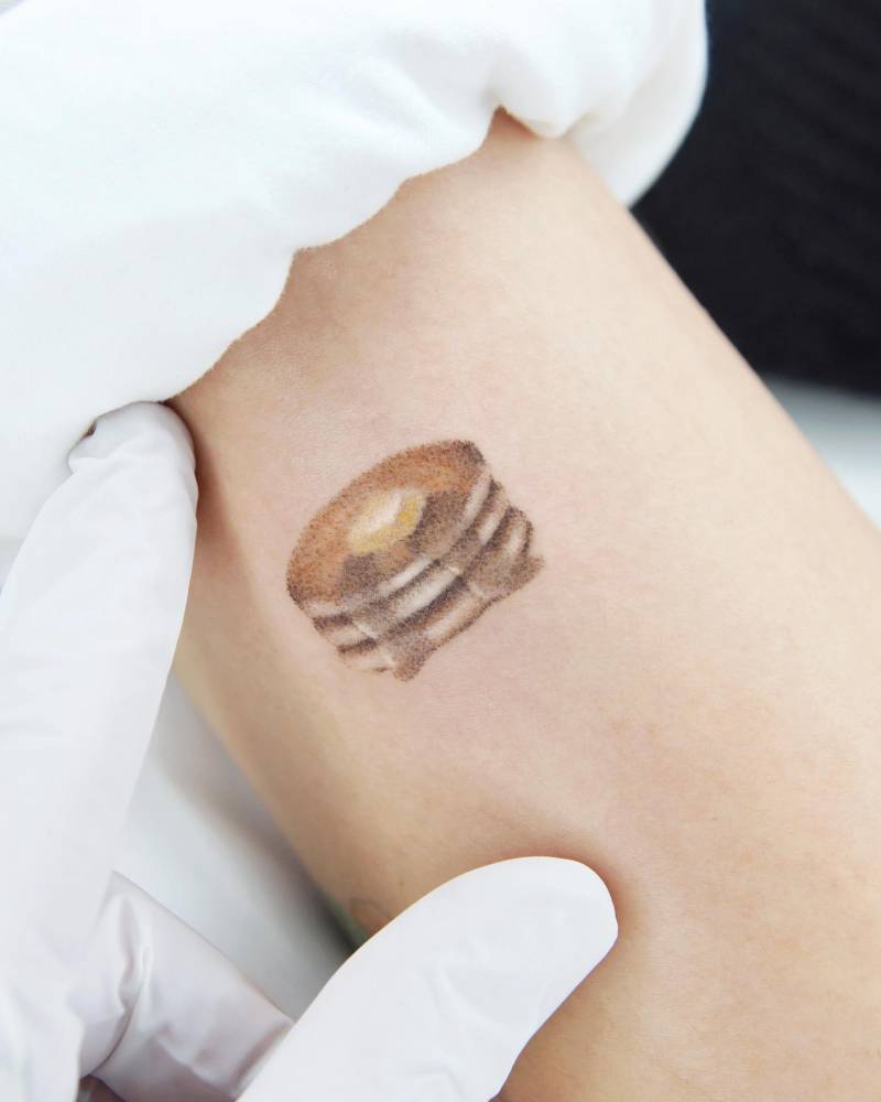 Hand poked pancakes tattoo located on the upper arm.