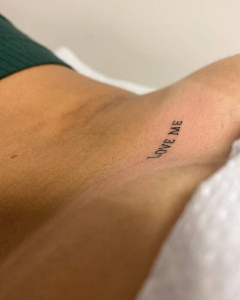 Tattoo that says "love me" located on the lower back.