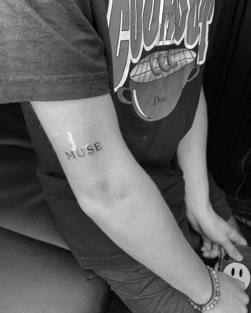 Tattoo of the word "muse" located on the tricep.