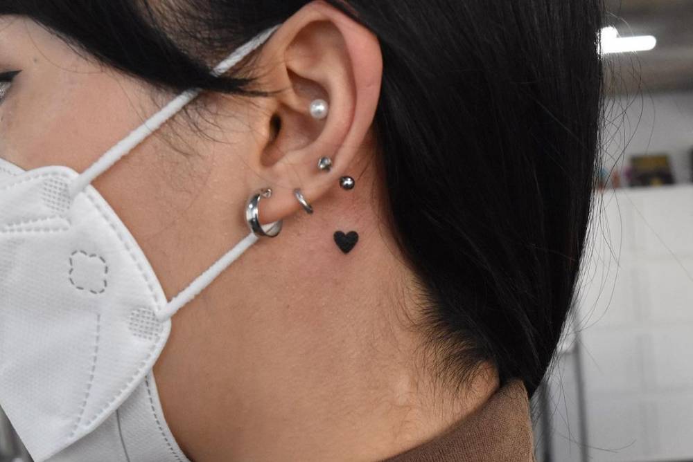 Minimalistic style heart tattoo located behind the ear.