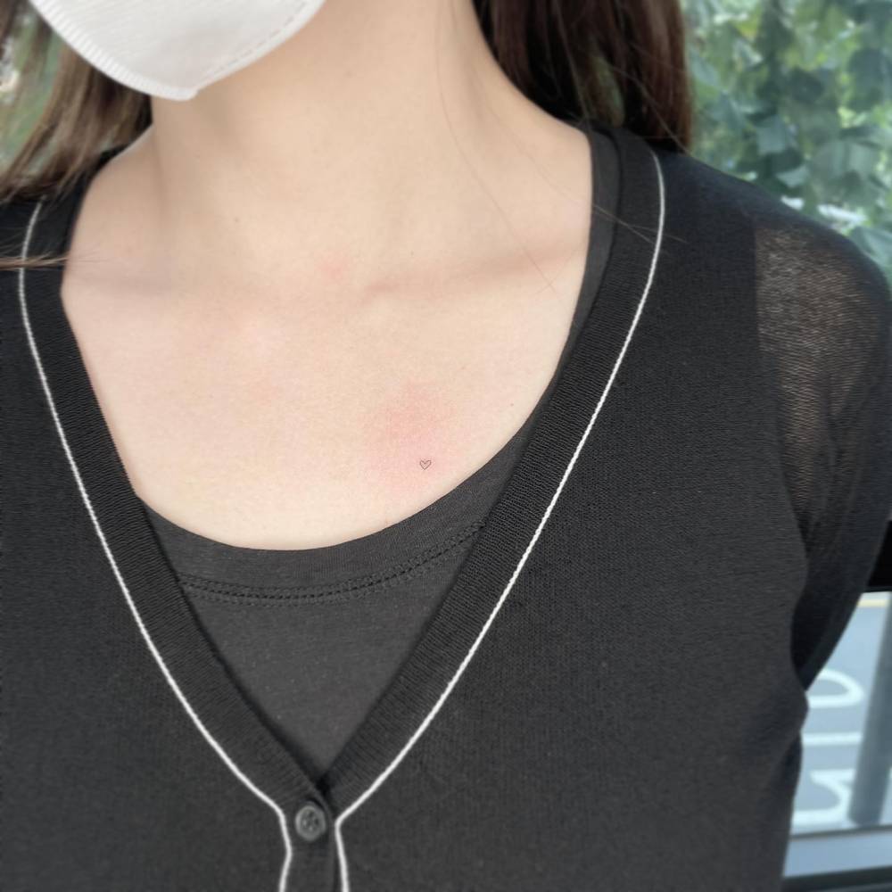 Micro heart tattoo located on the chest, minimalistic style.