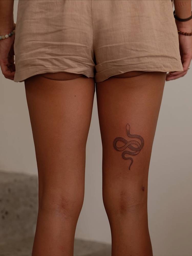 Snake tattoo in fine line style located on the thigh.