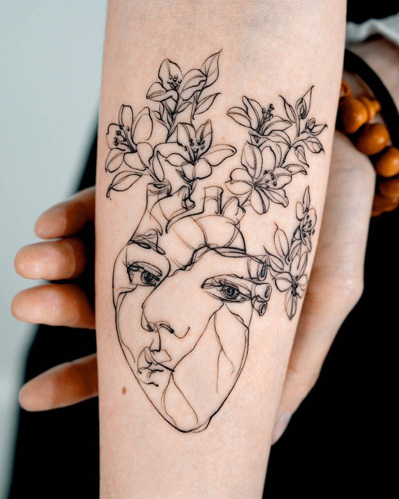 Flower head woman and anatomical heart tattoo located on the inner forearm.