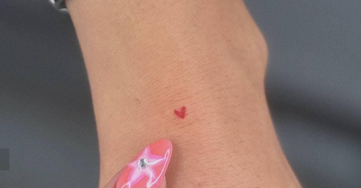 Tiny minimalistic red heart tattoo located on the
