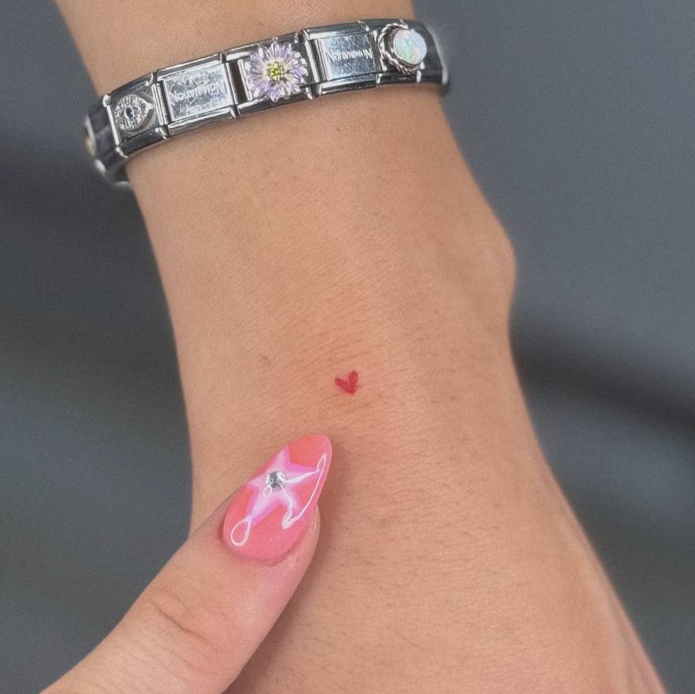 Tiny minimalistic red heart tattoo located on the wrist.