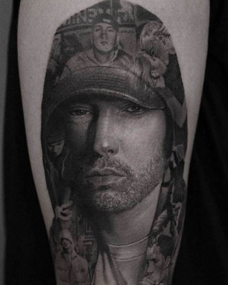 ‘Eminem’ portrait tattoo in black and grey style located on the upper arm.