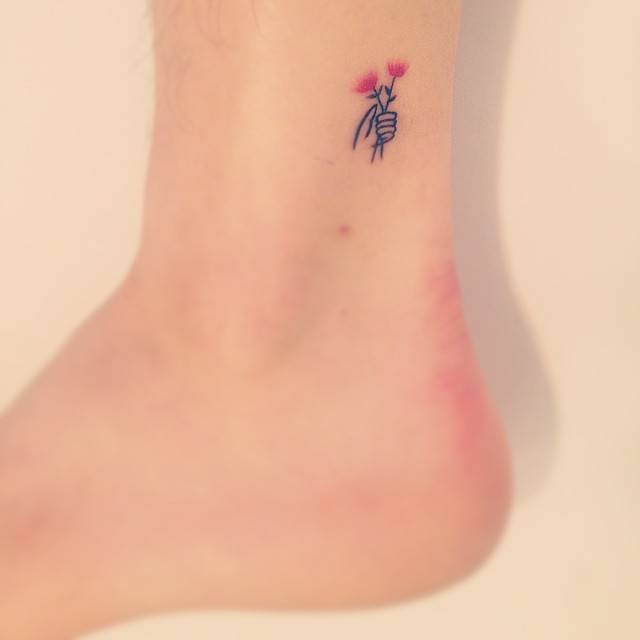 Tiny hand holding flowers tattoo in minimalistic style located on the ankle.