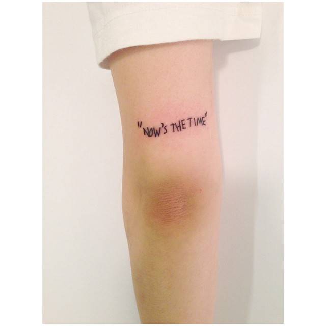 "Now's the time" lettering tattoo in handwritten font.