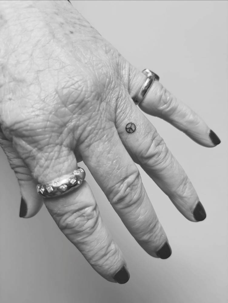 Micro peace symbol tattoo located on the finger, done in minimalistic style.