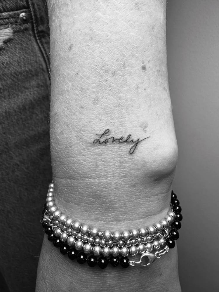 Handwritten font word "lovely" tattooed on the wrist.