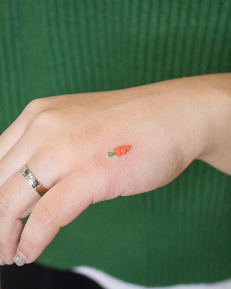 Tiny carrot emoji tattoo located on the hand.