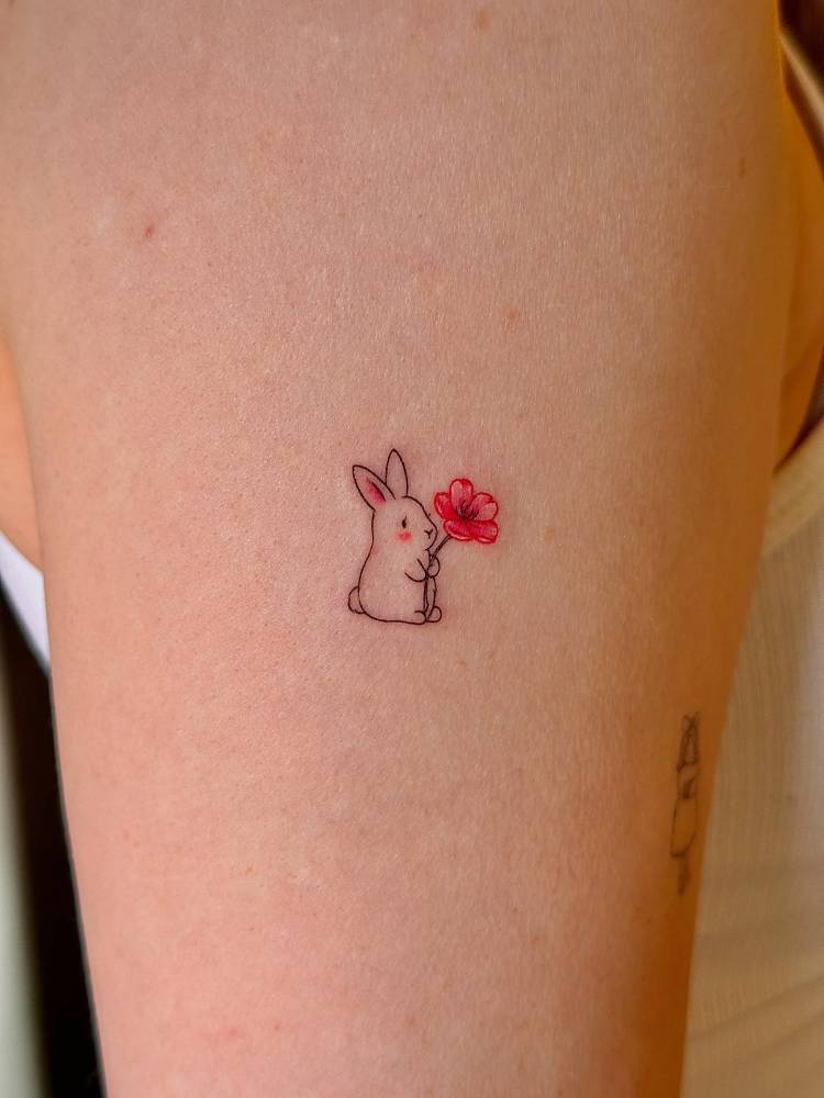Tiny bunny and cherry blossom tattoo located on the upper arm.