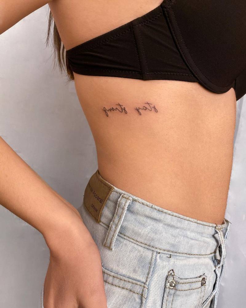 Mirror writing "stay strong" lettering tattoo on the rib.