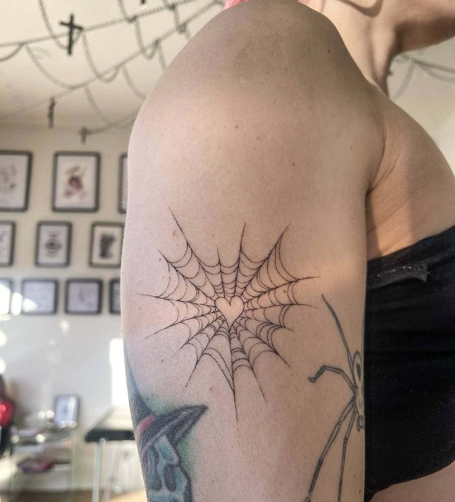 Spiderweb heart tattoo located on the upper arm, fine line style.