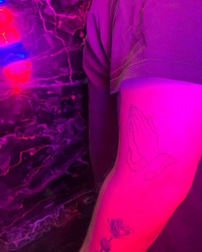 Durer's 'Praying Hands' tattoo in fine line style located on the upper arm.