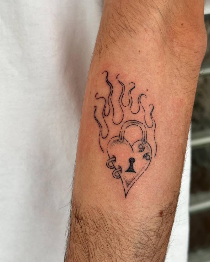 Flaming heart padlock tattoo located on the forearm.