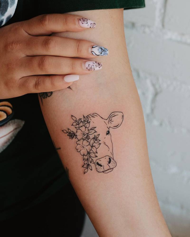 Fine line style cow portrait and flowers tattooed on the inner forearm.