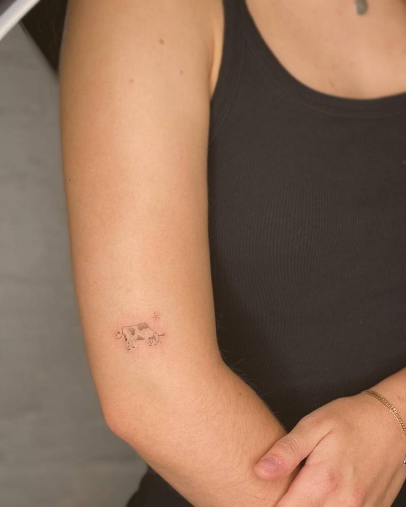 Minimalistic style mini cow tattoo located on the upper arm.