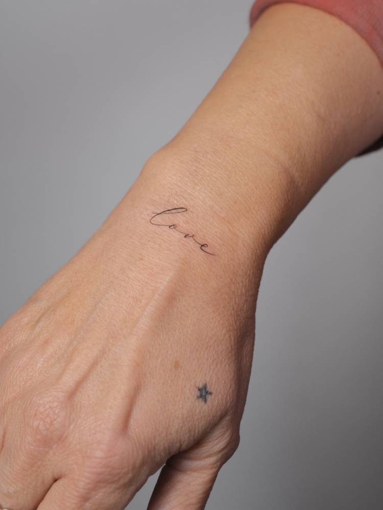 Script font word "love" tattooed on the wrist.