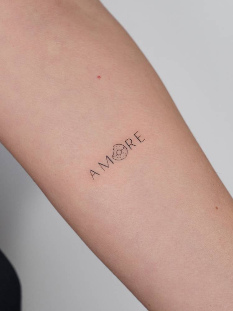 Word "amore" and little donut tattoo located on the inner forearm.