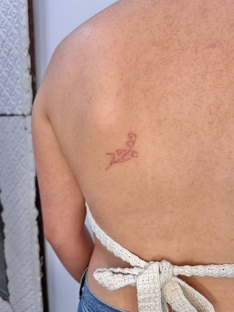 Single needle lily of the valley flowers tattoo located on the shoulder blade.