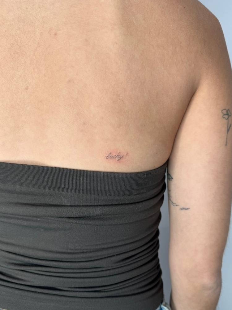 Handwritten font word "lucky" tattoo located on the back.