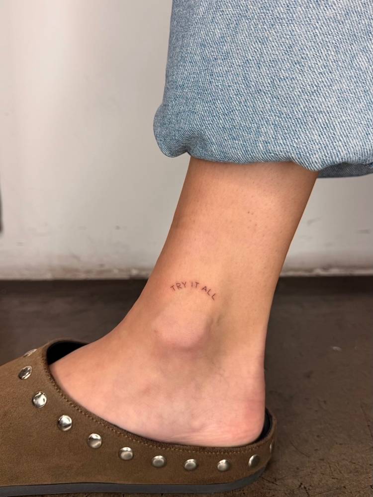 "Try it all" lettering tattoo located on the ankle.