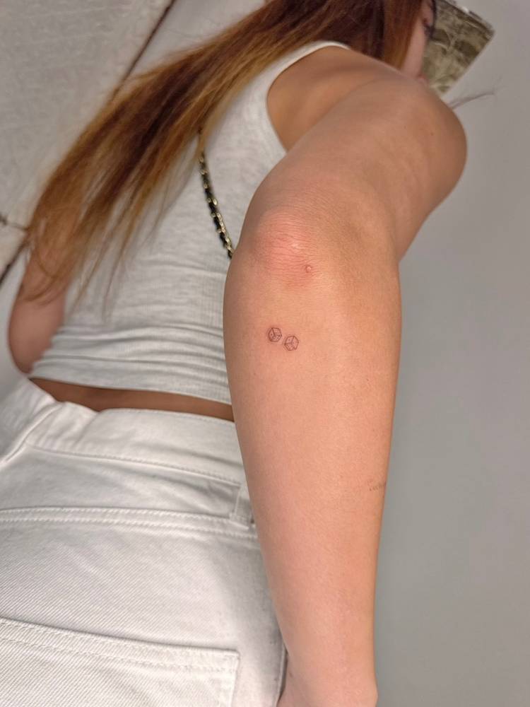 Little dice couple tattoo in fine line style located on the elbow.
