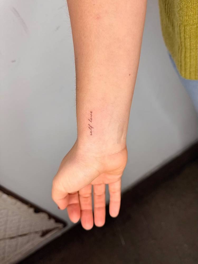 Lettering tattoo that says "self love" located on the wrist.
