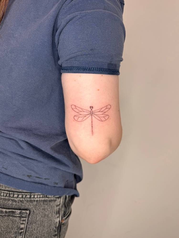 Dragonfly tattoo in fine line style placed on the tricep.