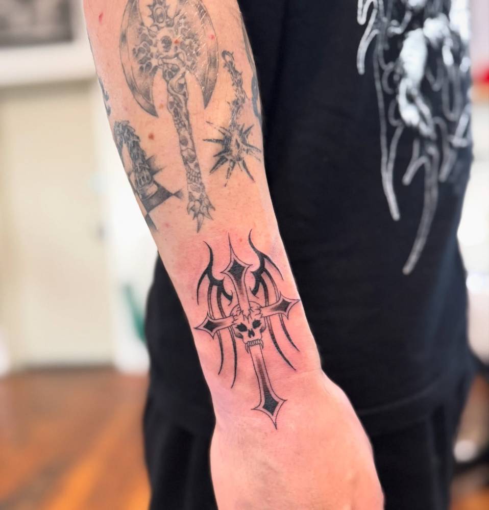 Tribal, cross and skull tattoo located on the wrist, illustrative style.
