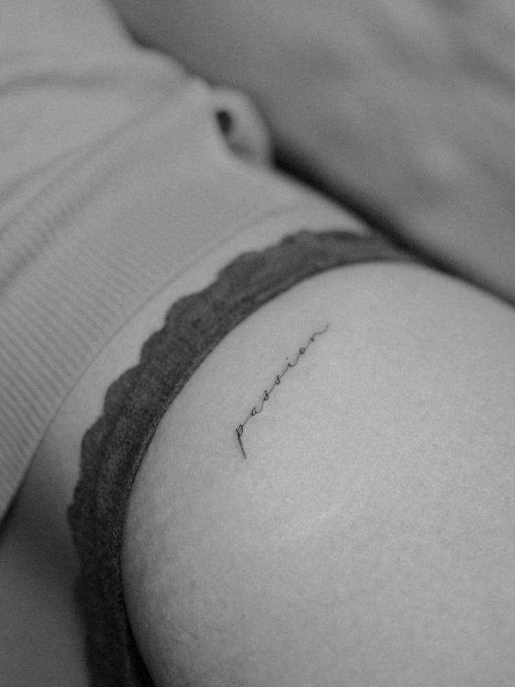 Lettering tattoo that says "passion" located on the hip.