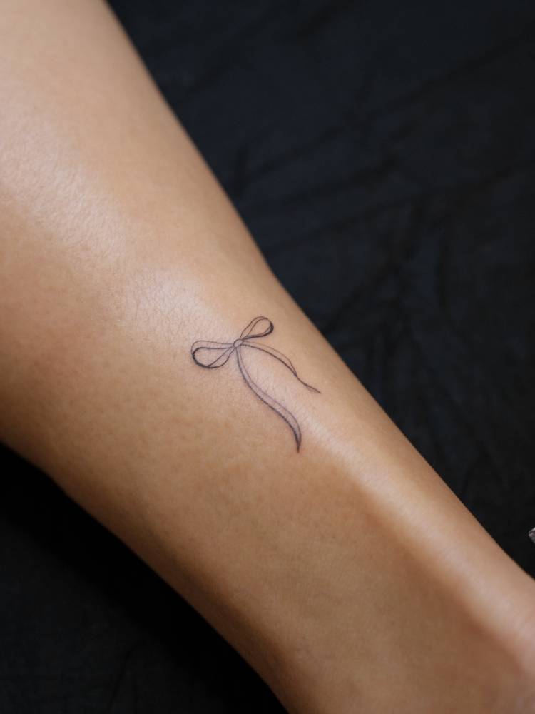 Ribbon bow tattoo located on the achilles, fine line style.