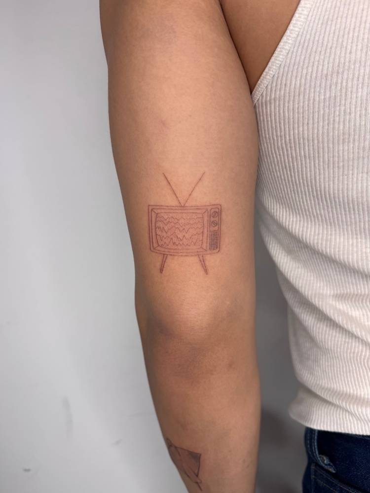 TV tattoo in fine line style located on the tricep.