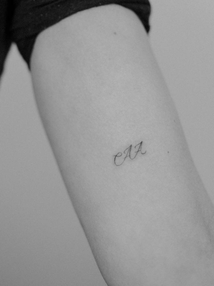 Initials tattoo in script font located on the inner arm.