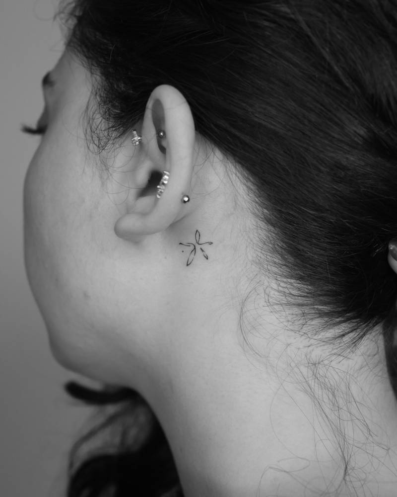 Tiny minimalistic tattoo of a flower located behind the ear.