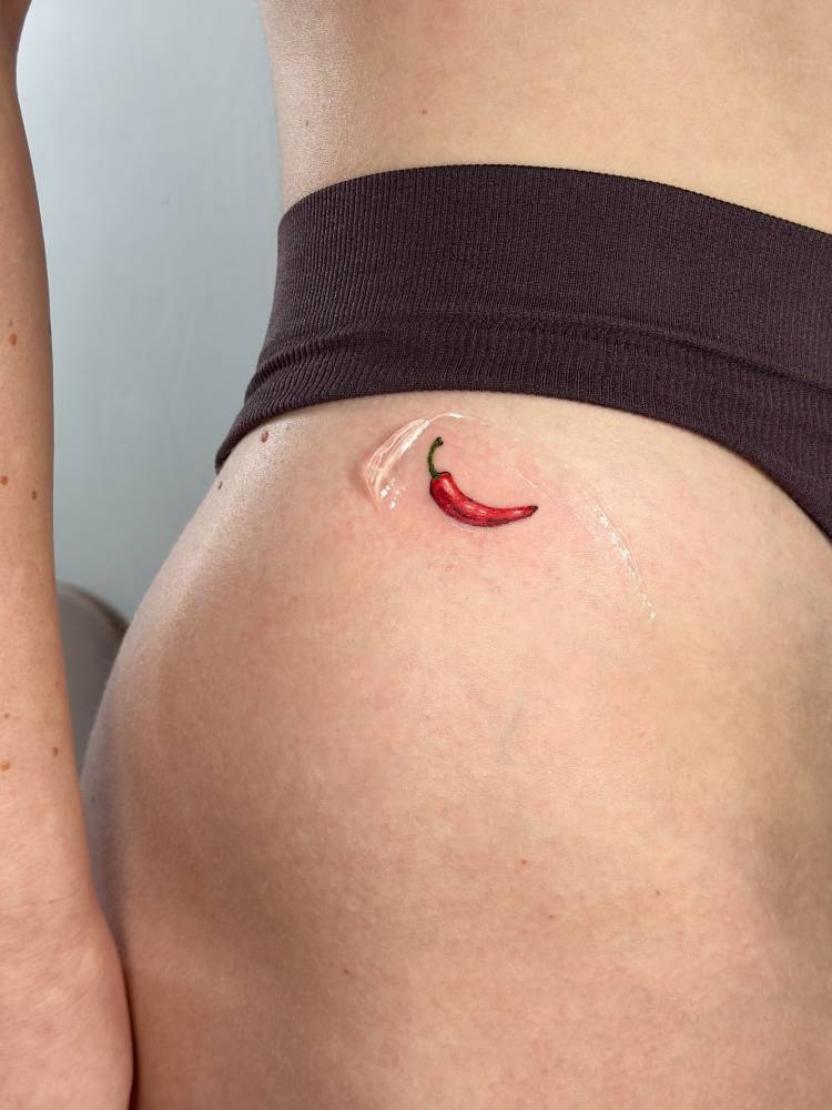 Red chili tattoo located on the hip, done in illustrative style.