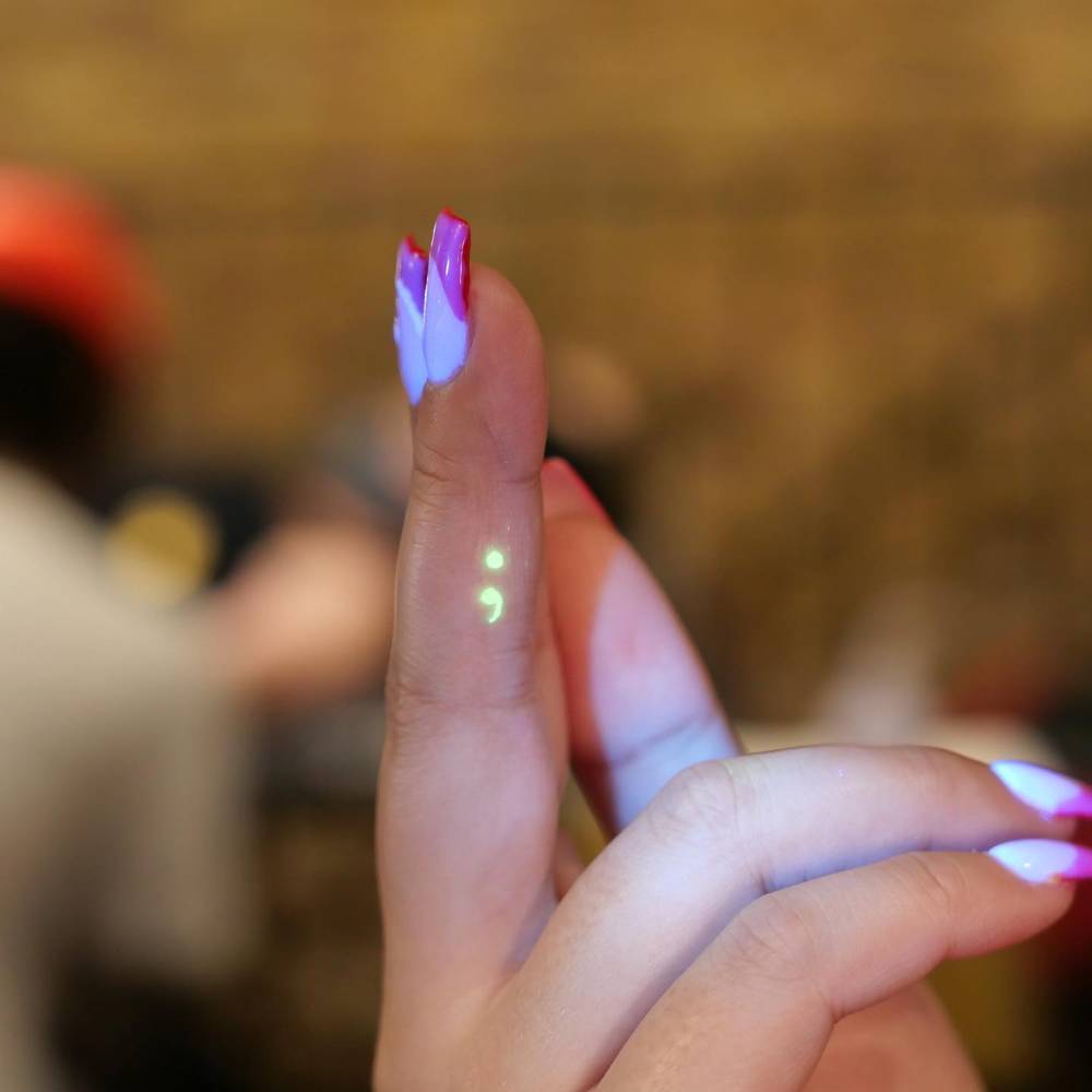 UV ink semicolon tattoo located on the finger.
