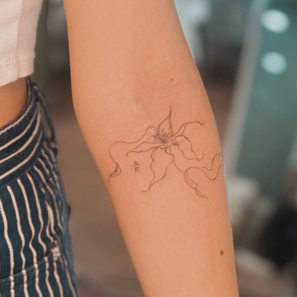 Lily flower tattoo in fine line style located on the inner forearm.