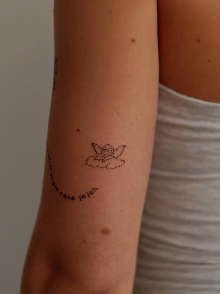 Sleeping cherub in fine line style tattooed on the tricep.